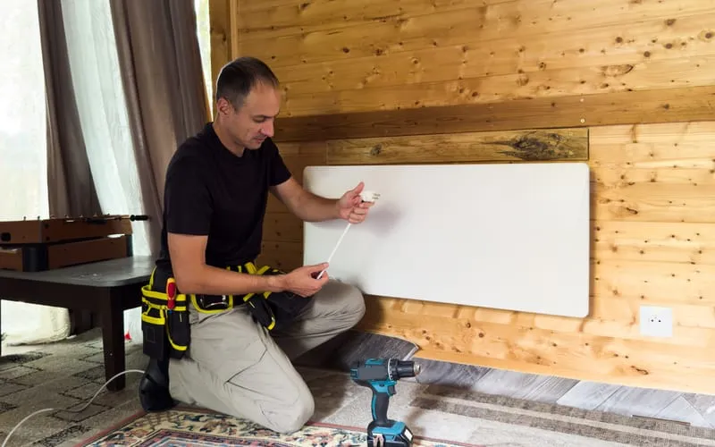 Installateur fixant un panneau rayonnant électrique sur un mur.