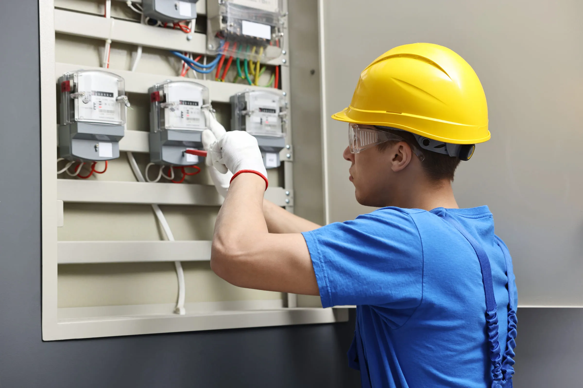 Électricien casqué intervenant sur un tableau électrique.