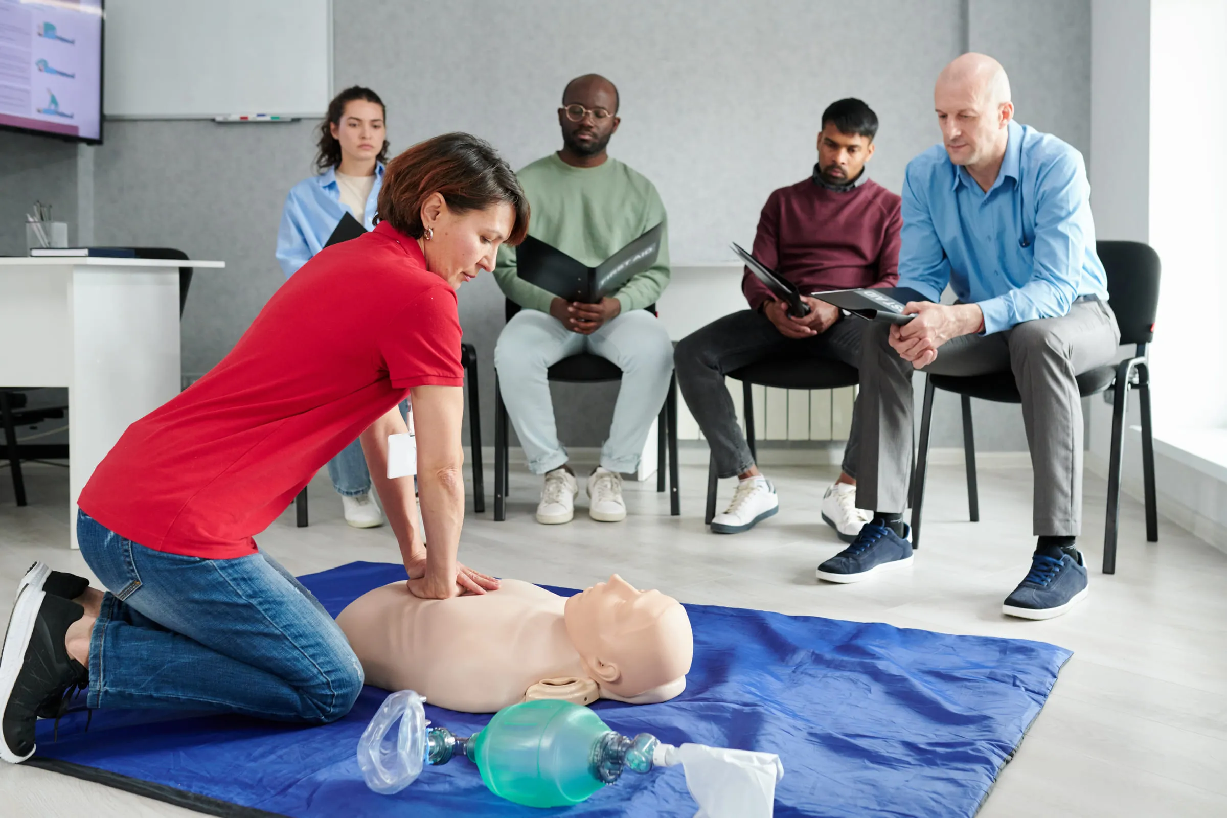 Formatrice démontrant un massage cardiaque sur mannequin devant un groupe de stagiaires.