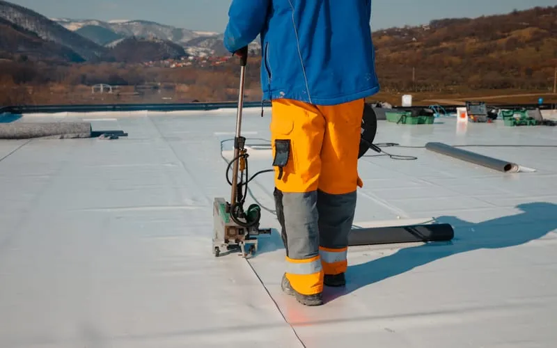 Étancheur déroulant une membrane sur une toiture terrasse.