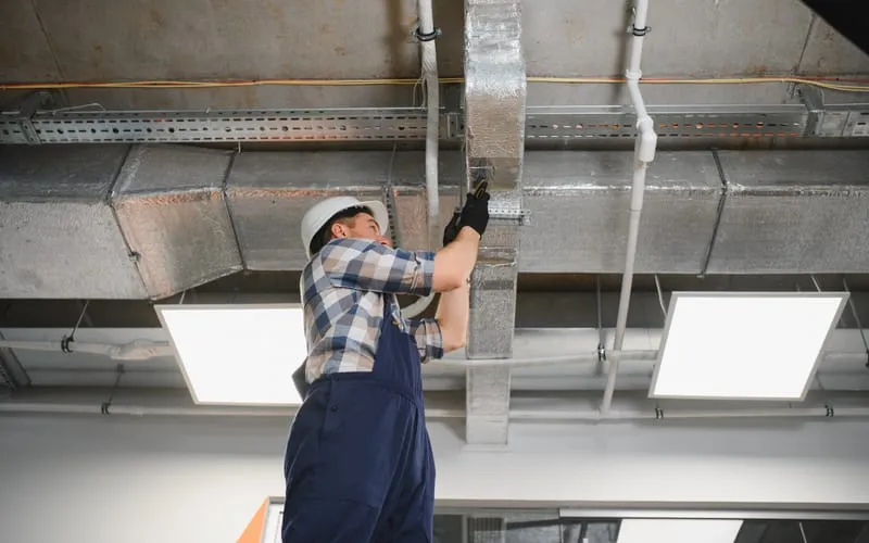 Technicien intervenant sur un réseau de gaines de ventilation.